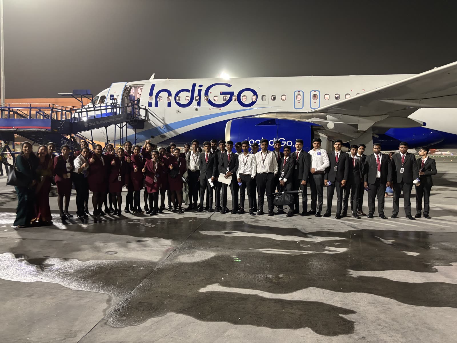 Students lined up on the apron beside an IndiGo Airbus A320 at night