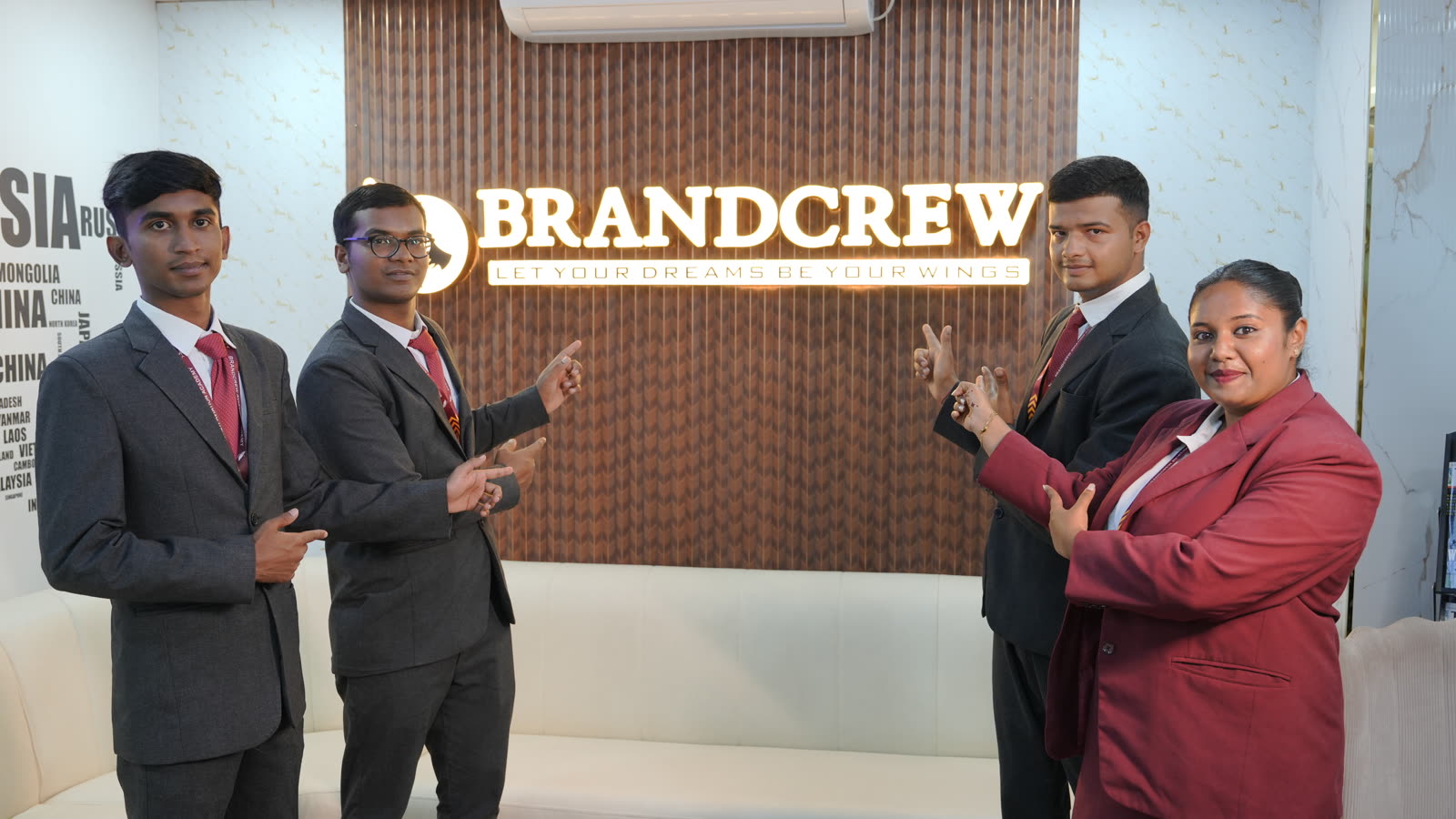 Four students in uniform pointing proudly at the glowing Brandcrew sign above the reception sofa