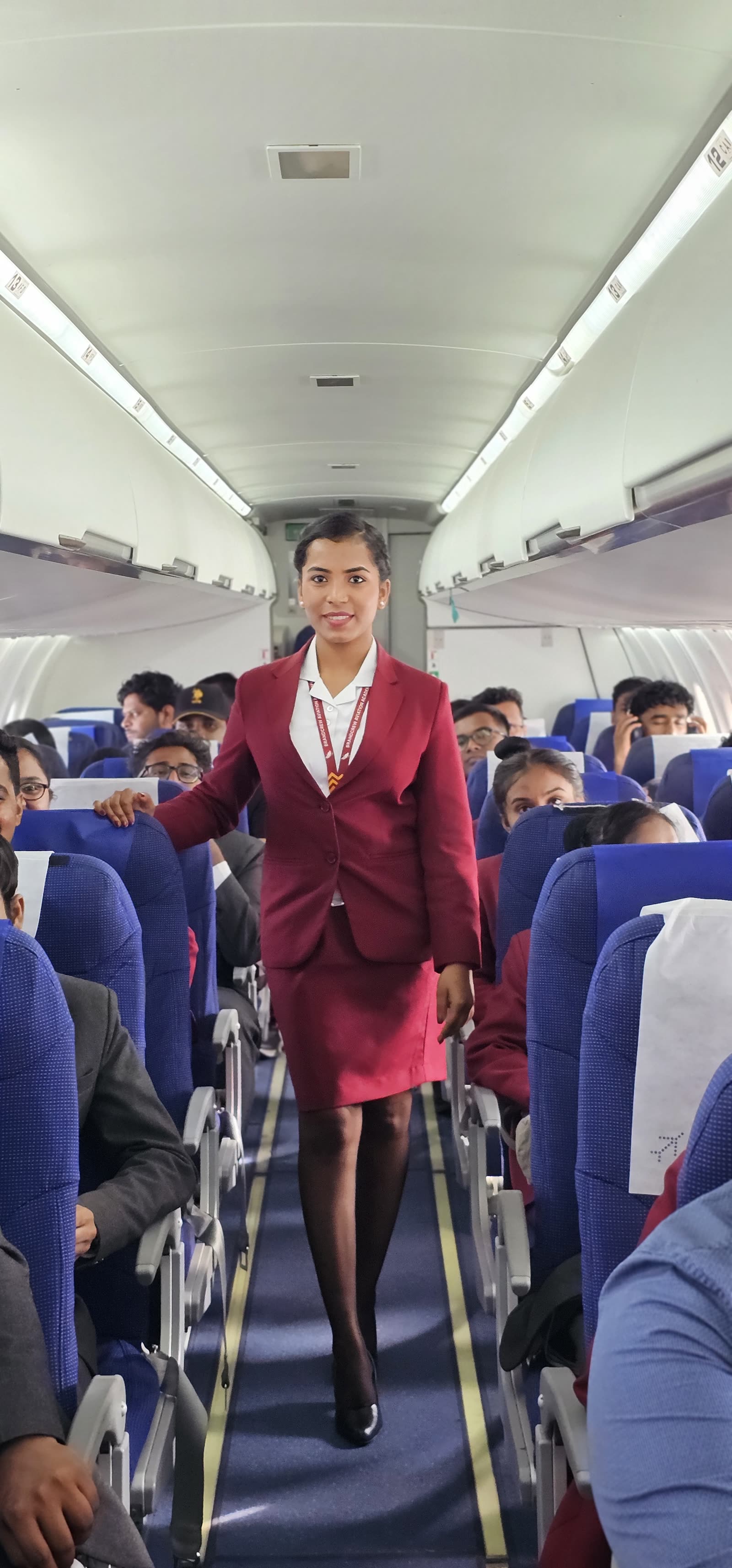 A cabin crew trainee walking the aisle of a full aircraft cabin