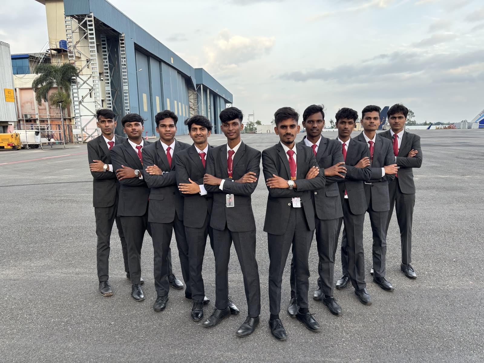 Ten male students in suits in front of the hangar at dusk