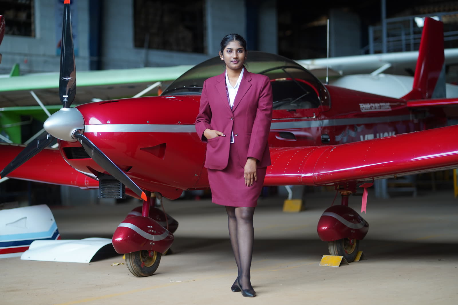 A trainee standing in front of a red trainer aircraft propeller