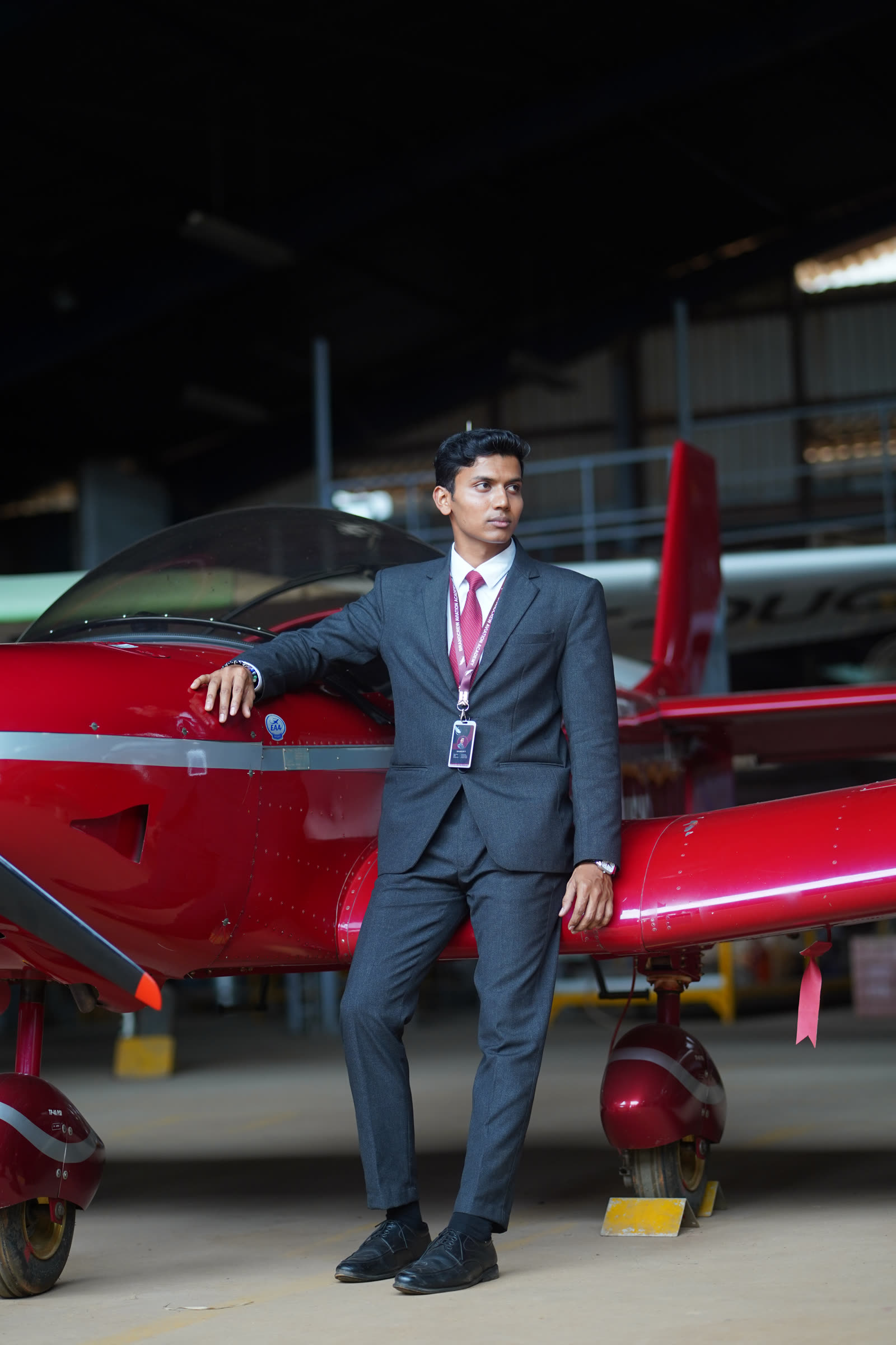 A student resting a hand on the canopy of a red trainer aircraft