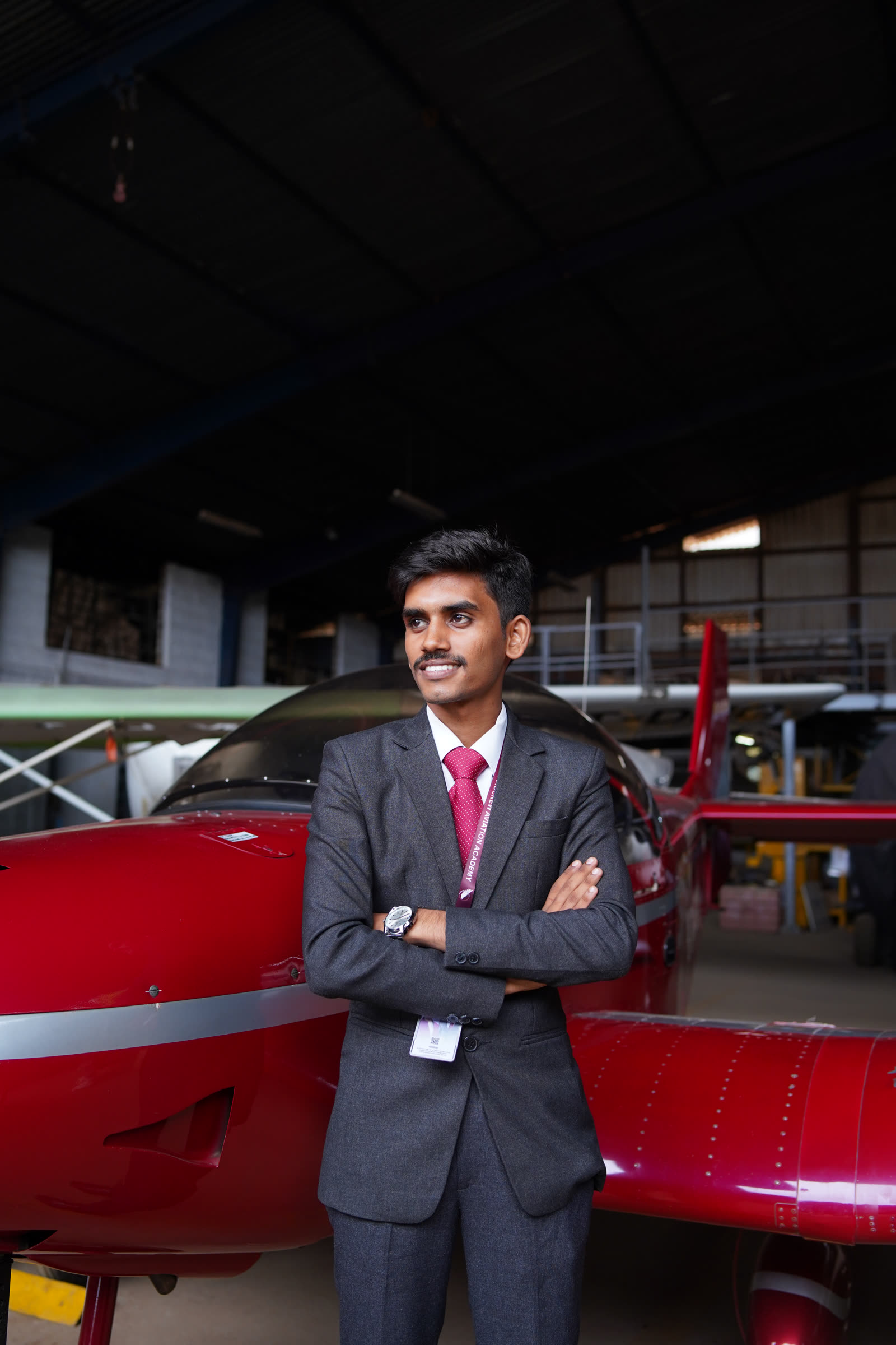 A student in a suit beside a red trainer aircraft in the hangar