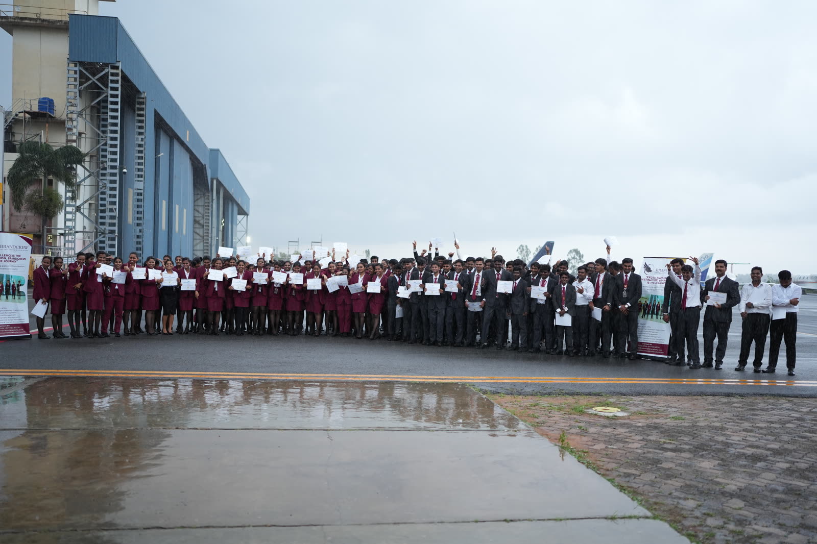 The cohort holding their certificates in front of the hangars